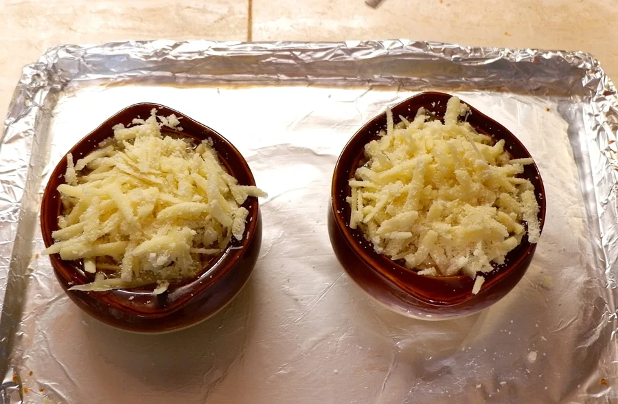 Deux bols de soupe à l'oignon couverts de fromage râpé, posés sur une plaque avant de passer au four