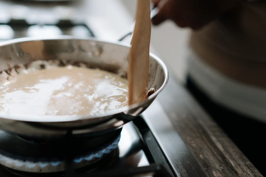Sauce brune liée dans une sauteuse en inox, remuée avec une spatule en bois sur un feu de cuisinière