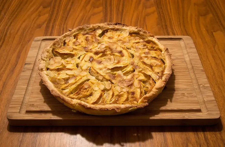 Tarte normande aux pommes et amandes effilées, crème dorée prise entre les quartiers, sur une planche en bois